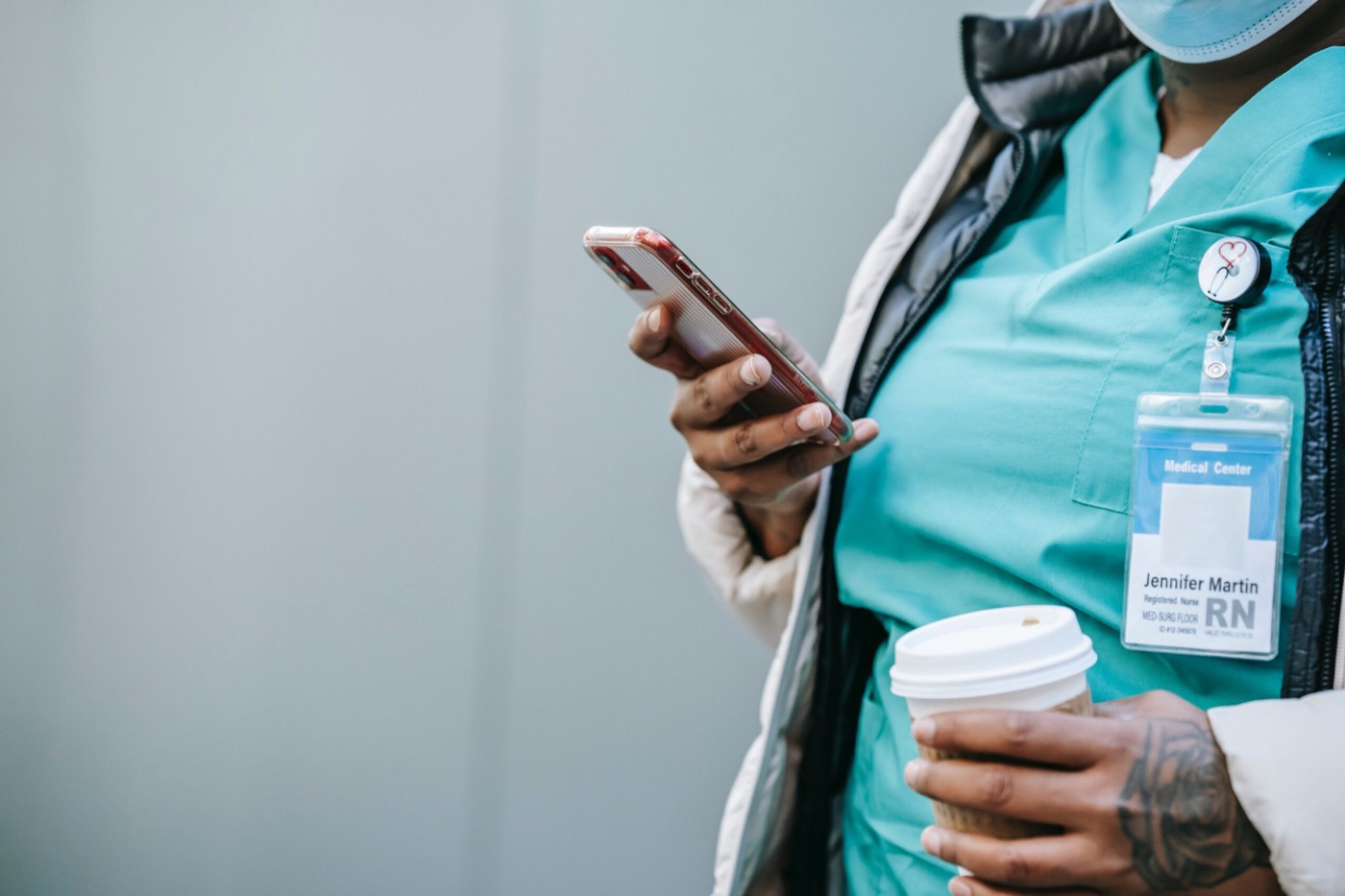 Un’infermiera consulta lo smartphone con un caffè in mano